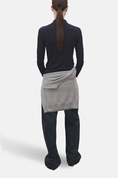 T-shirt à manches longues bleu de MANGO, porté avec un pull gris noué autour de la taille et un jean foncé.