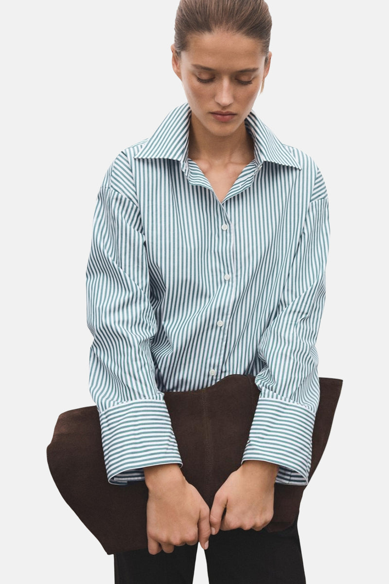 Chemise à manches longues verte rayée de MANGO, portée avec un pantalon noir et tenant un sac marron.