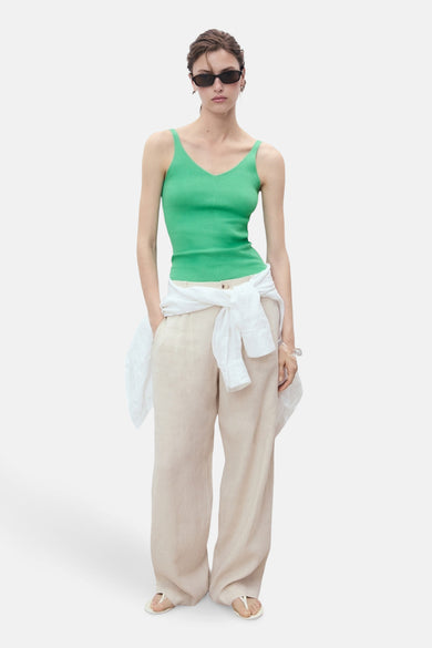 Débardeur vert de MANGO, porté avec un pantalon beige ample et une chemise blanche nouée à la taille.