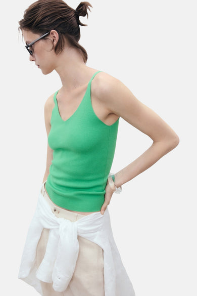 Débardeur vert côtelé de MANGO, porté avec une chemise blanche nouée à la taille.