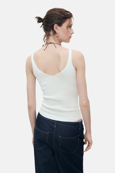 Witte tanktop van MANGO, gedragen met een donkerblauwe broek, van achteren gezien, met een zwarte ketting.