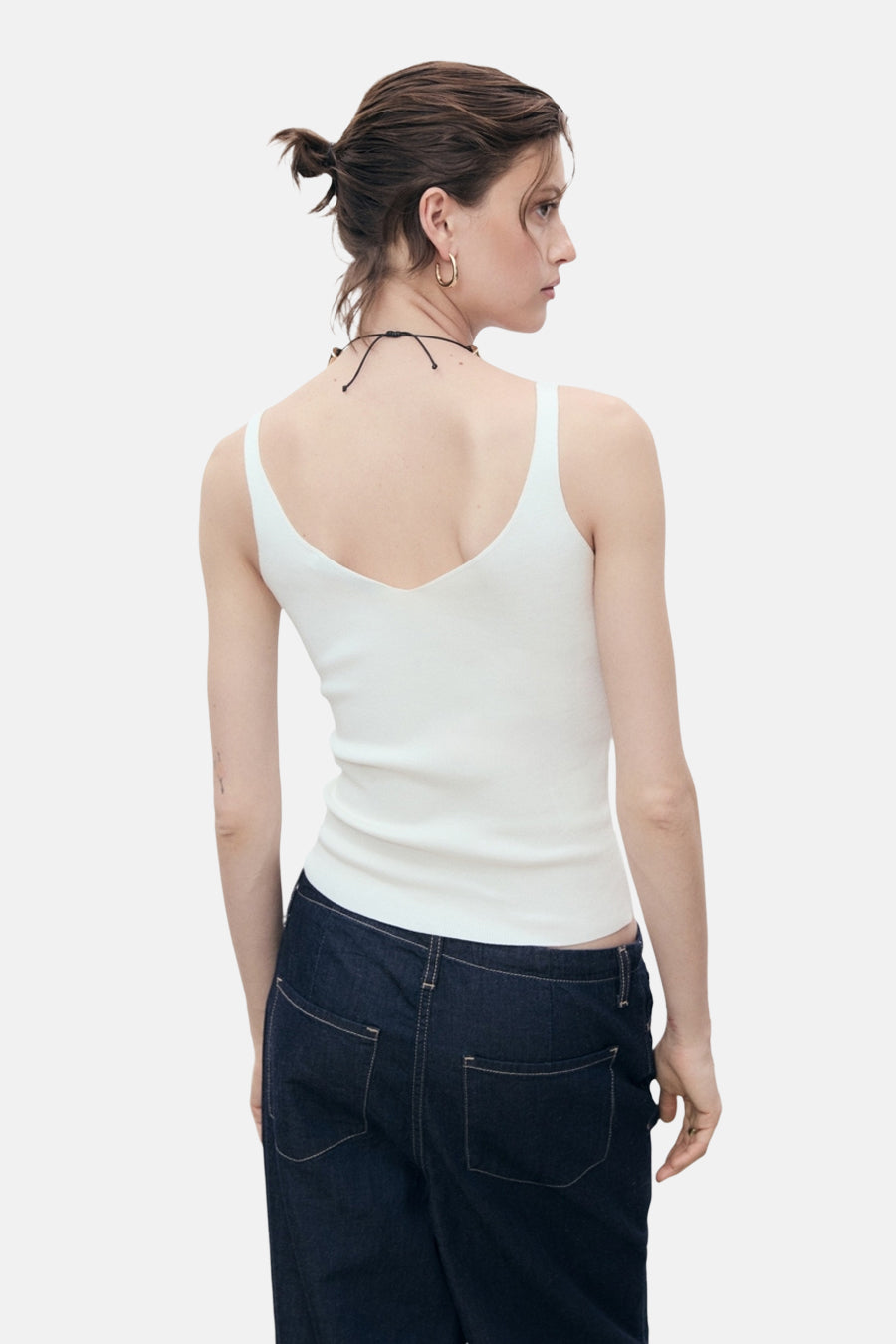 Witte tanktop van MANGO, gedragen met een donkerblauwe broek, van achteren gezien, met een zwarte ketting.