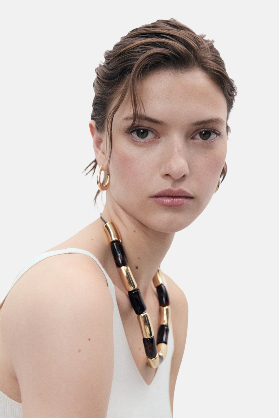 Witte tanktop van MANGO, gedragen met een ketting met grote kralen en gouden oorbellen.