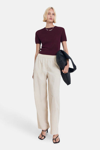 Bordeaux ronde hals trui van MANGO, gedragen met een beige high-waist broek, zwarte sandalen en een zwarte gevlochten tas.