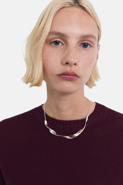 Pull à col rond bordeaux de MANGO, porté avec un collier argenté minimaliste.