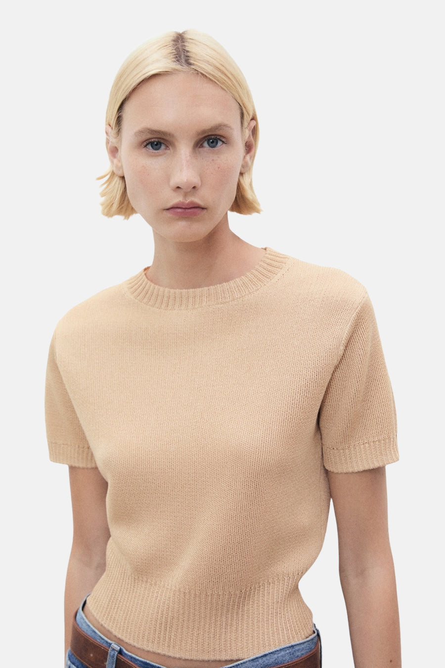 Beige trui met ronde hals van MANGO, in fijne breinaalden, gedragen met een spijkerbroek en een bruine riem.