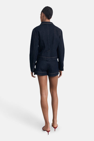 Bermuda en denim bleu foncé de MANGO, porté avec une veste en jean assortie et des mules rouges.