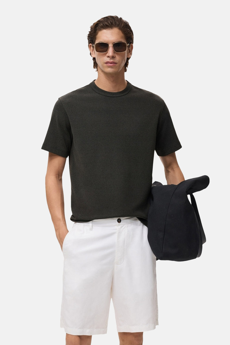 Zwart T-shirt met korte mouwen van MANGO, gedragen met een witte bermuda en een zwarte jas over de schouder.