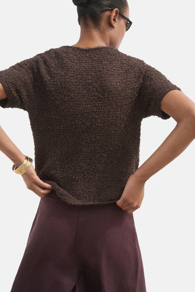 Cardigan brun de MANGO avec une texture bouclée, porté avec un pantalon prune et des bracelets dorés.