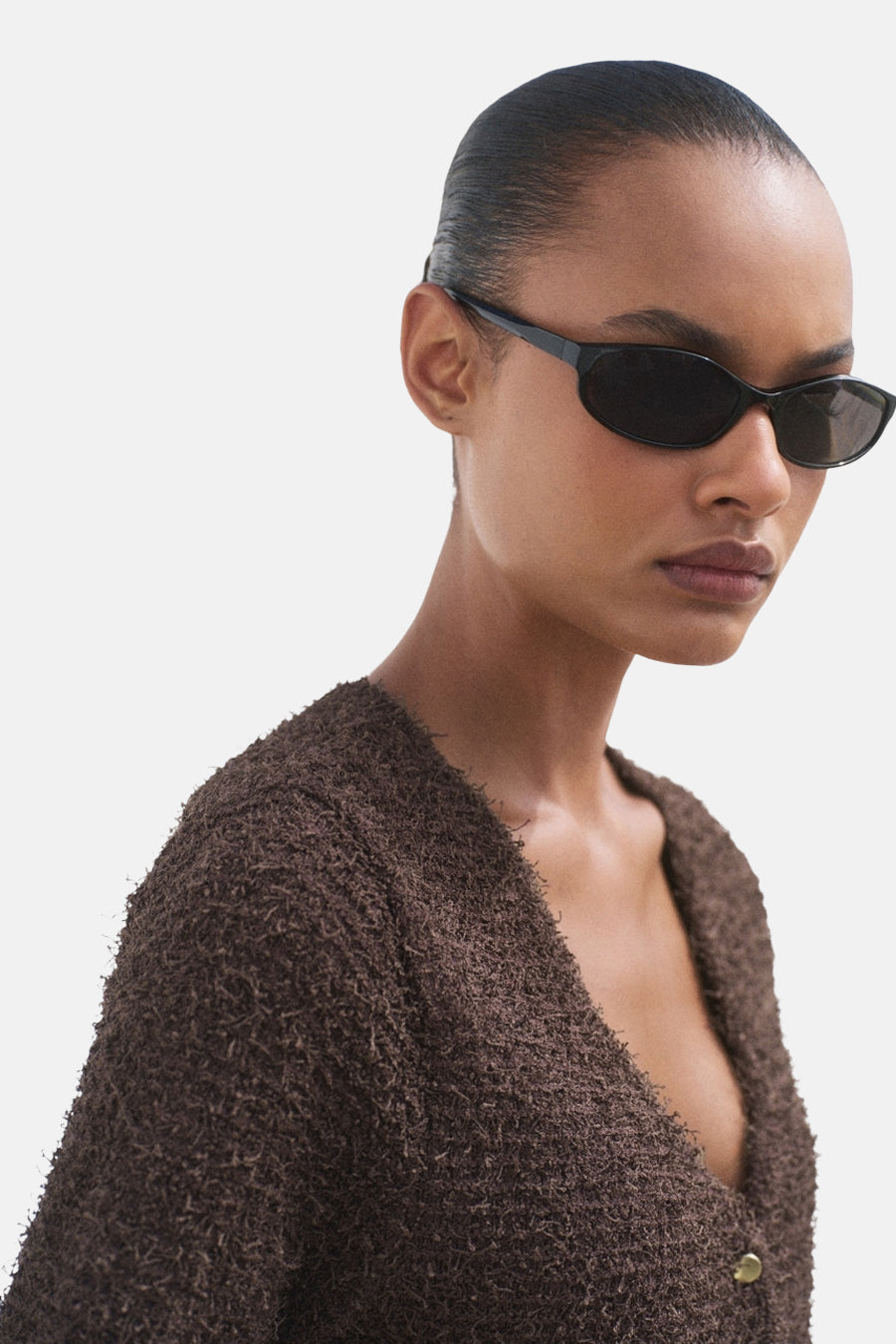 Cardigan marron de MANGO, en texture bouclée, porté avec des lunettes de soleil noires.
