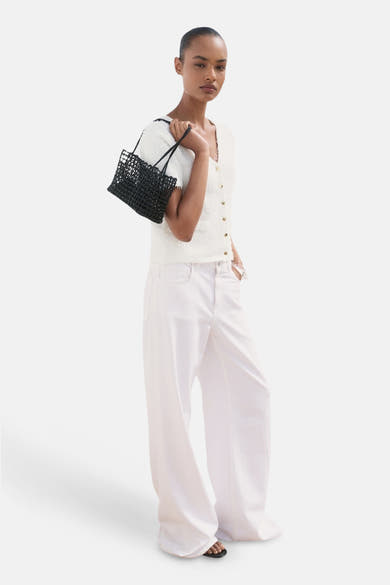 Cardigan blanc du MANGO avec boutons dorés, porté avec un pantalon blanc ample et un sac noir tressé.