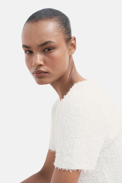 Cardigan blanc de MANGO, en maille texturée, porté avec un maquillage neutre et des cheveux tirés vers l'arrière.