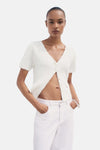 Cardigan blanc en maille texturée par MANGO, porté ouvert avec un jean blanc et un bracelet transparent.