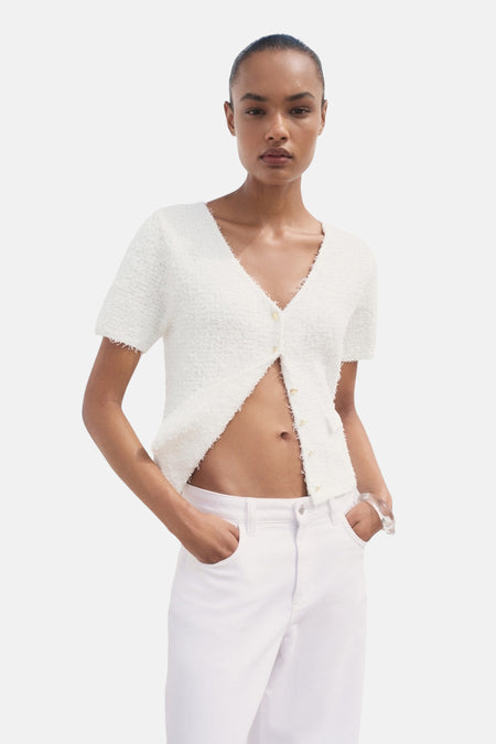 Witte cardigan van MANGO in bouclébrei, gedragen met een bikini en een witte jeans, met een transparante armband.