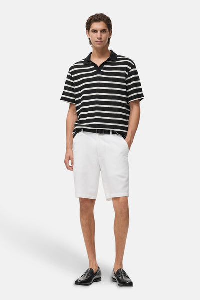 Zwart gestreept poloshirt van MANGO, gedragen met een witte korte broek en zwarte loafers.