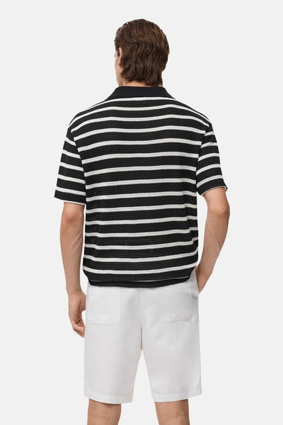 Zwart poloshirt met korte mouwen van MANGO, met witte horizontale strepen en gedragen met een witte korte broek.