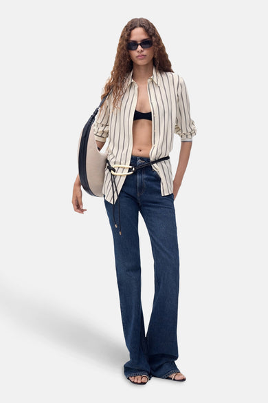 Chemise beige à rayures par MANGO, portée ouverte avec un soutien-gorge noir et un jean taille haute.