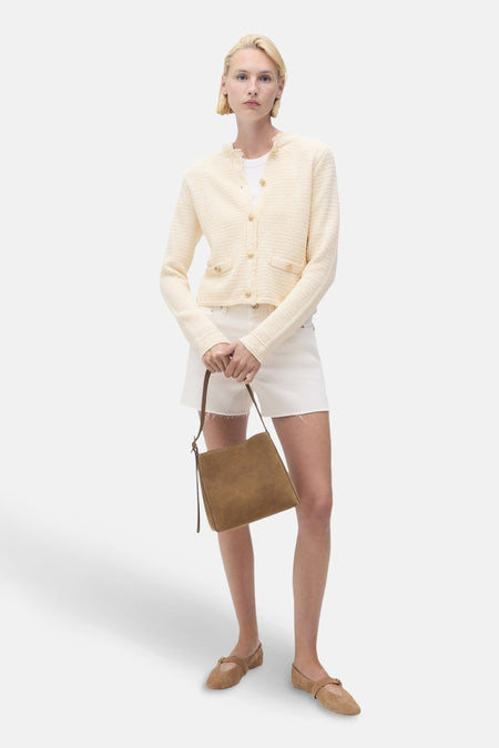 Ecru vest van MANGO, in een getextureerde breinaard met opgestikte zakken, gedragen met een witte korte broek en platte schoenen.