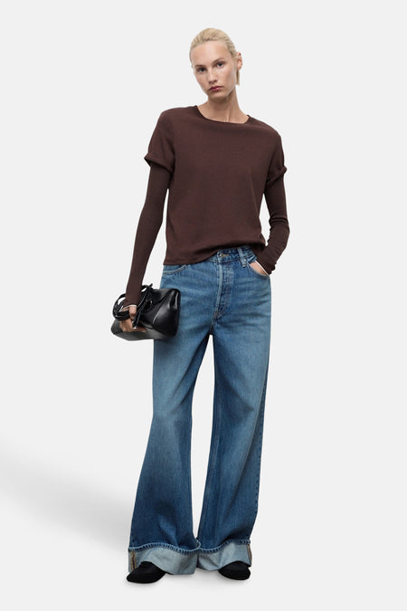 Jean large en denim bleu moyen de MANGO, porté avec un t-shirt marron et un sac noir.

