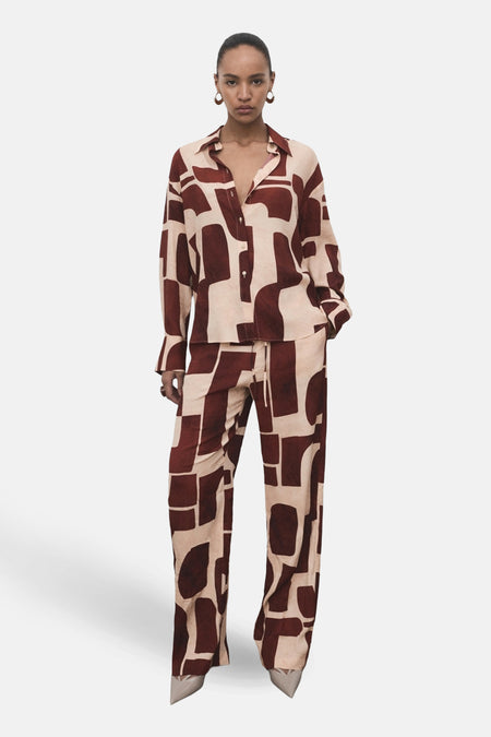 Chemise à manches longues multicolore de MANGO, à motif géométrique marron et beige, portée avec un pantalon assorti.