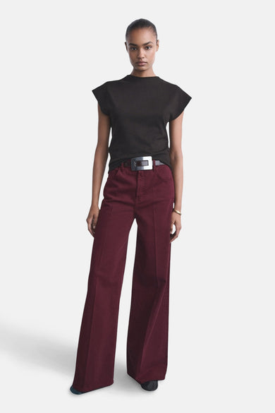 Jeans coloré bordeaux de MANGO, pantalon large porté avec un T-shirt noir et une ceinture à boucle argentée.