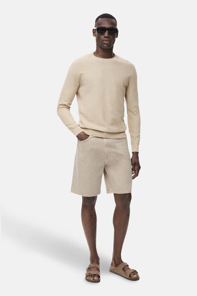 Pull à col rond beige de MANGO, porté avec un short en jean et des sandales à double bride.