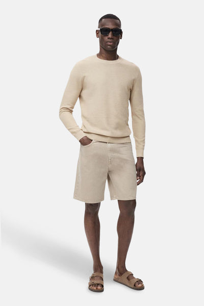 Pull à col rond beige de MANGO, porté avec un short en jean et des sandales à double bride.