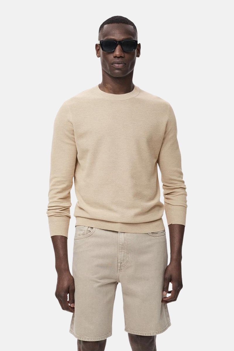 Pull à col rond beige de MANGO, porté avec un short assorti et des lunettes de soleil noires.
