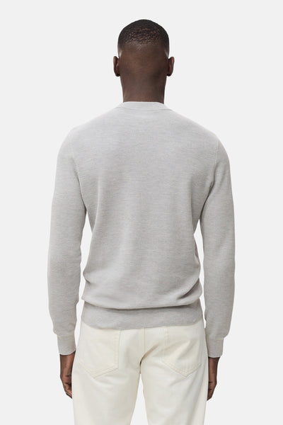 Grijze trui met ronde hals van MANGO, in een getextureerde breinaard, gedragen met een gebroken witte broek, achterzicht.