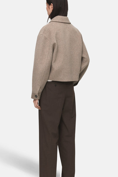 Korte beige jas van MANGO, met knopen en lange mouwen, gedragen met een bruine broek.
