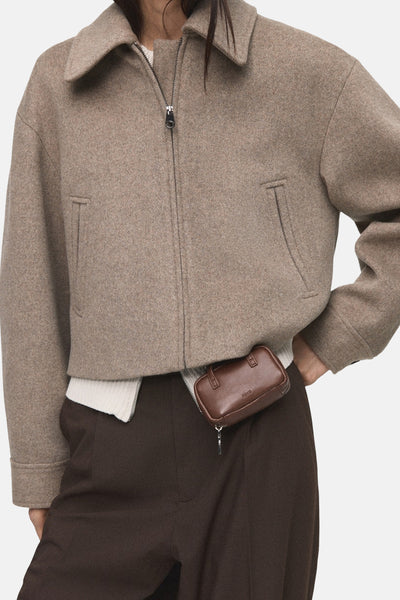 Korte beige jas van MANGO, met ritssluiting en zakken, gedragen met een bruine broek.