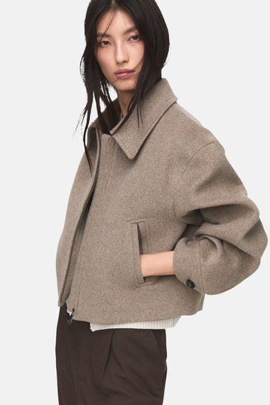 Korte beige jas van MANGO, met ritssluiting en zakken, gedragen met een bruine broek.
