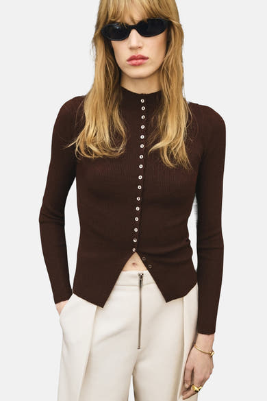 Bruin geribd gebreid vest van MANGO, met knoopsluiting aan de voorkant, gedragen met een witte broek met hoge taille.