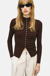 Bruin geribd gebreid vest van MANGO, met knoopsluiting aan de voorkant, gedragen met een witte broek met hoge taille.