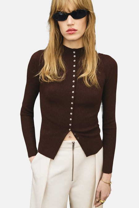 Bruin geribd gebreid vest van MANGO, met knoopsluiting aan de voorkant, gedragen met een witte broek met hoge taille.
