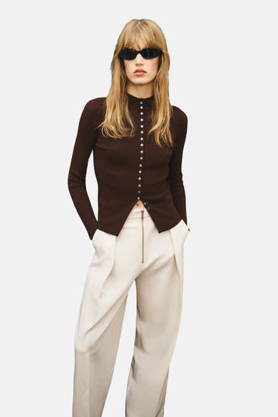 Bruin gilet van MANGO gedragen met een broek met hoge taille en zichtbare rits en een zonnebril.