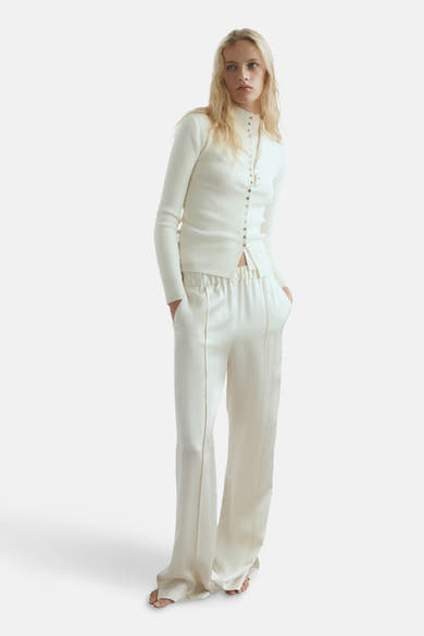 Gilet beige de MANGO, maille côtelée avec boutonnage sur le devant, porté avec un pantalon taille haute.