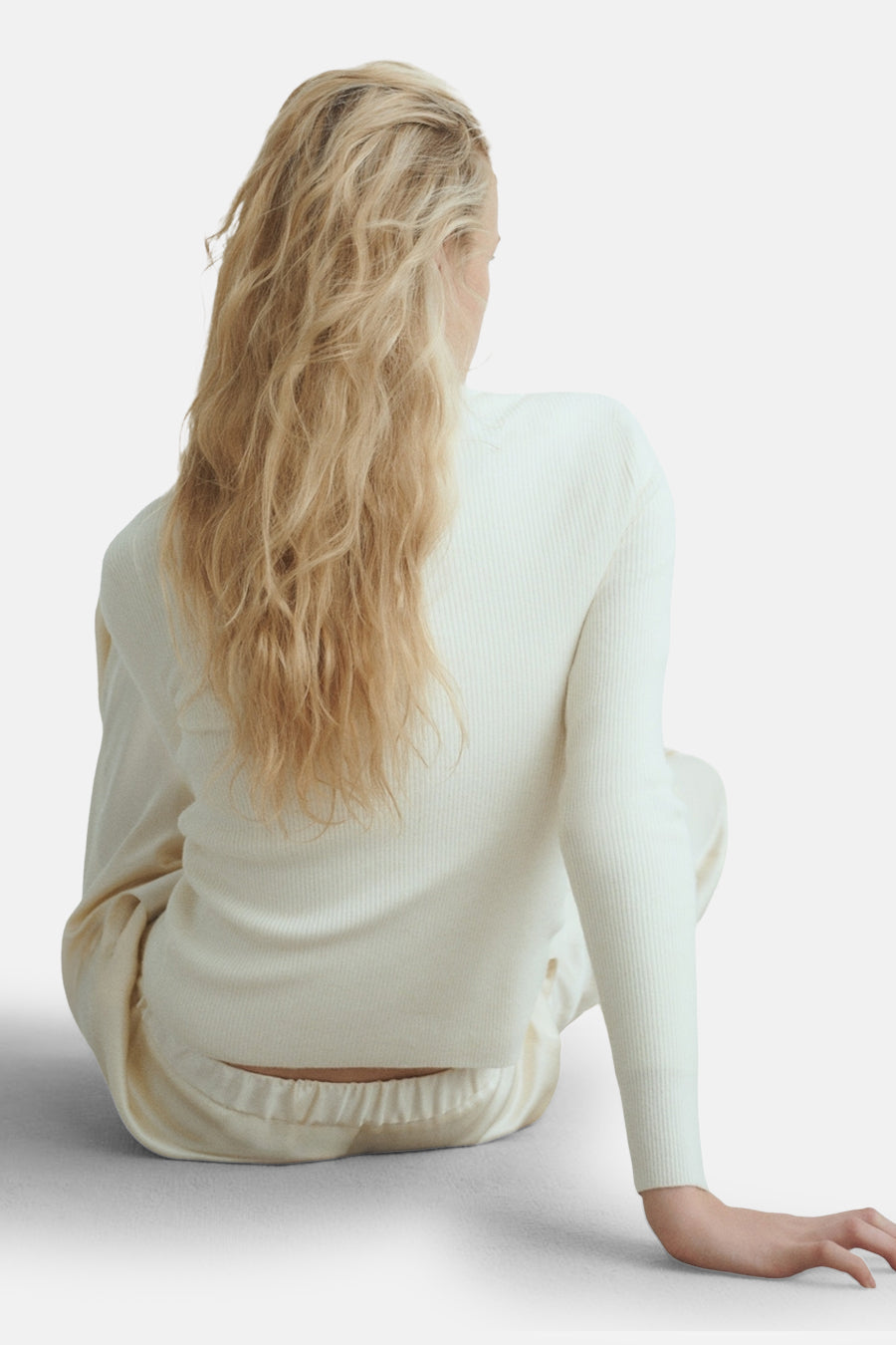 Gilet beige de MANGO, en maille côtelée, porté avec un pantalon de pyjama, vue de dos.
