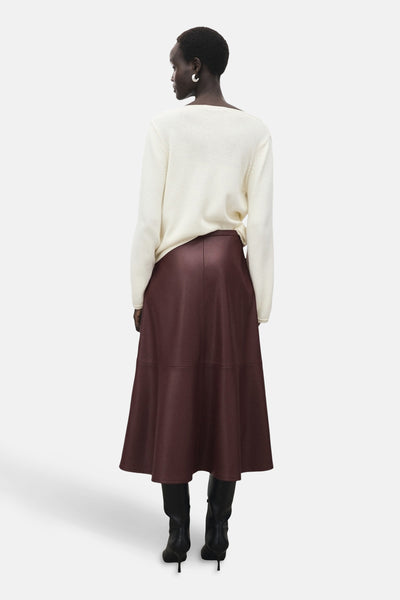 Jupe longue bordeaux par MANGO, portée avec un pull blanc et des bottes noires à talons, vue de dos.