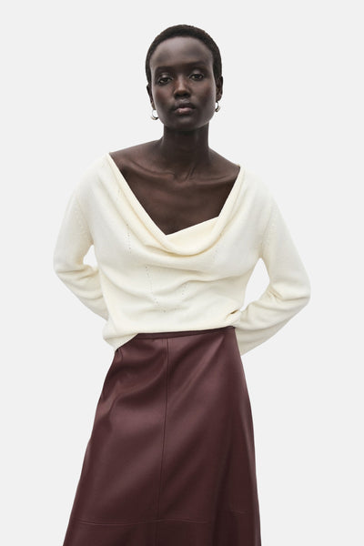 Jupe longue bordeaux de MANGO, coupe évasée, portée avec un pull blanc à col drapé et des boucles d'oreilles.