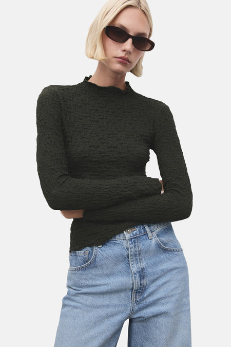 Kaki getextureerd T-shirt met lange mouwen van MANGO, rugdetail, gedragen met een blauwe jeans met hoge taille.