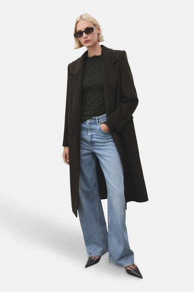 T-shirt kaki à manches longues de MANGO, porté avec un manteau long et un jean ample.