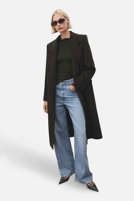 T-shirt kaki à manches longues de MANGO, porté avec un manteau long et un jean ample.