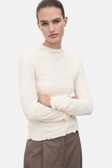 T-shirt à manches longues beige de MANGO, en tissu texturé, porté avec un pantalon marron.
