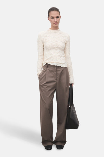 T-shirt beige à manches longues de MANGO, texture gaufrée, porté avec un pantalon marron et un sac noir.
