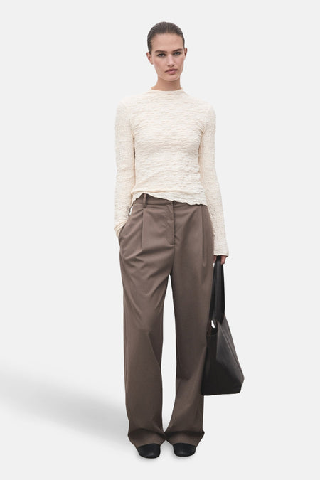 T-shirt beige à manches longues de MANGO, texture gaufrée, porté avec un pantalon marron et un sac noir.
