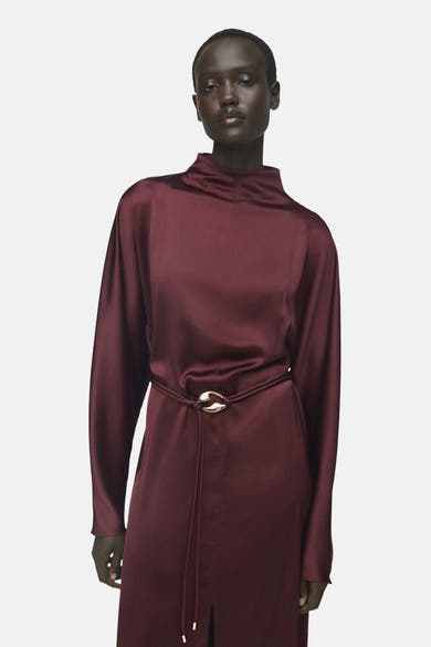 Robe bordeaux à manches longues de MANGO, avec une ceinture fine dorée à la taille.
