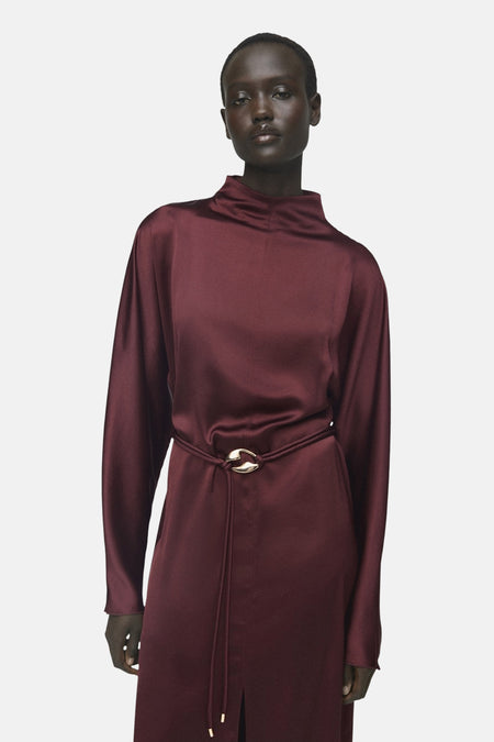 Robe bordeaux à manches longues de MANGO, avec une ceinture fine dorée à la taille.
