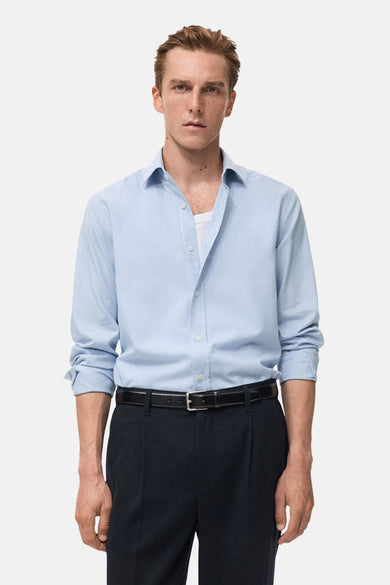 Chemise à manches longues bleue de MANGO, portée avec un pantalon de costume noir et une ceinture en cuir.