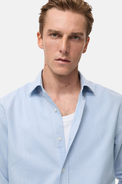 Chemise à manches longues bleue de MANGO, en coton texturé, portée ouverte sur un t-shirt blanc.
